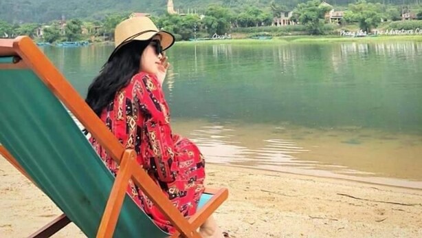 A person sitting on a beach chair by a lake with mountains in the background. - Areca Bungalow (Phong Nha)