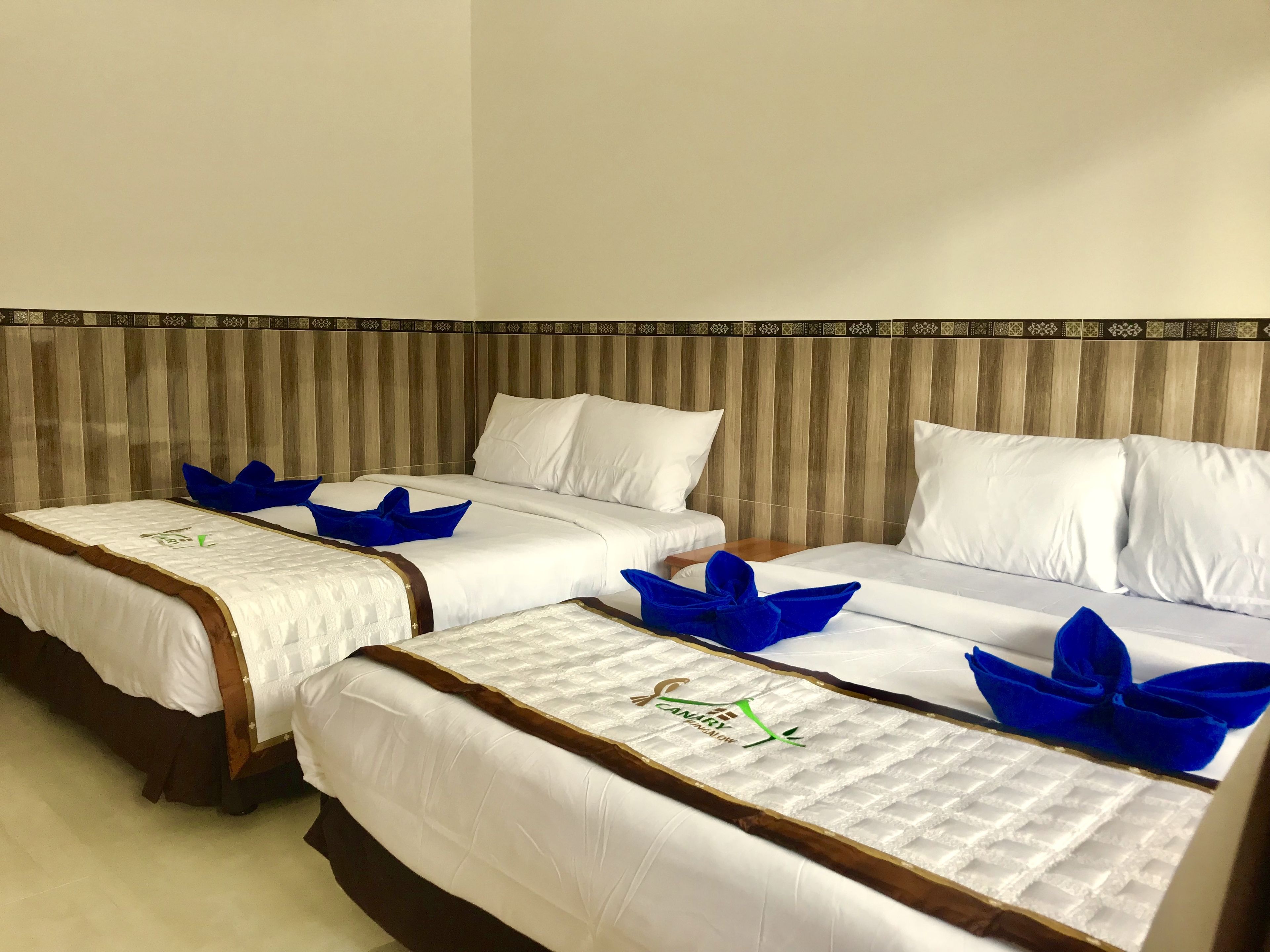 A hotel room with three beds, each with white bedding and blue decorative pillows.