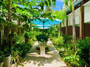 A narrow pathway flanked by lush greenery and a blue umbrella, leading to a building with a tiled exterior. - Canary Bungalow (Phu Quoc)