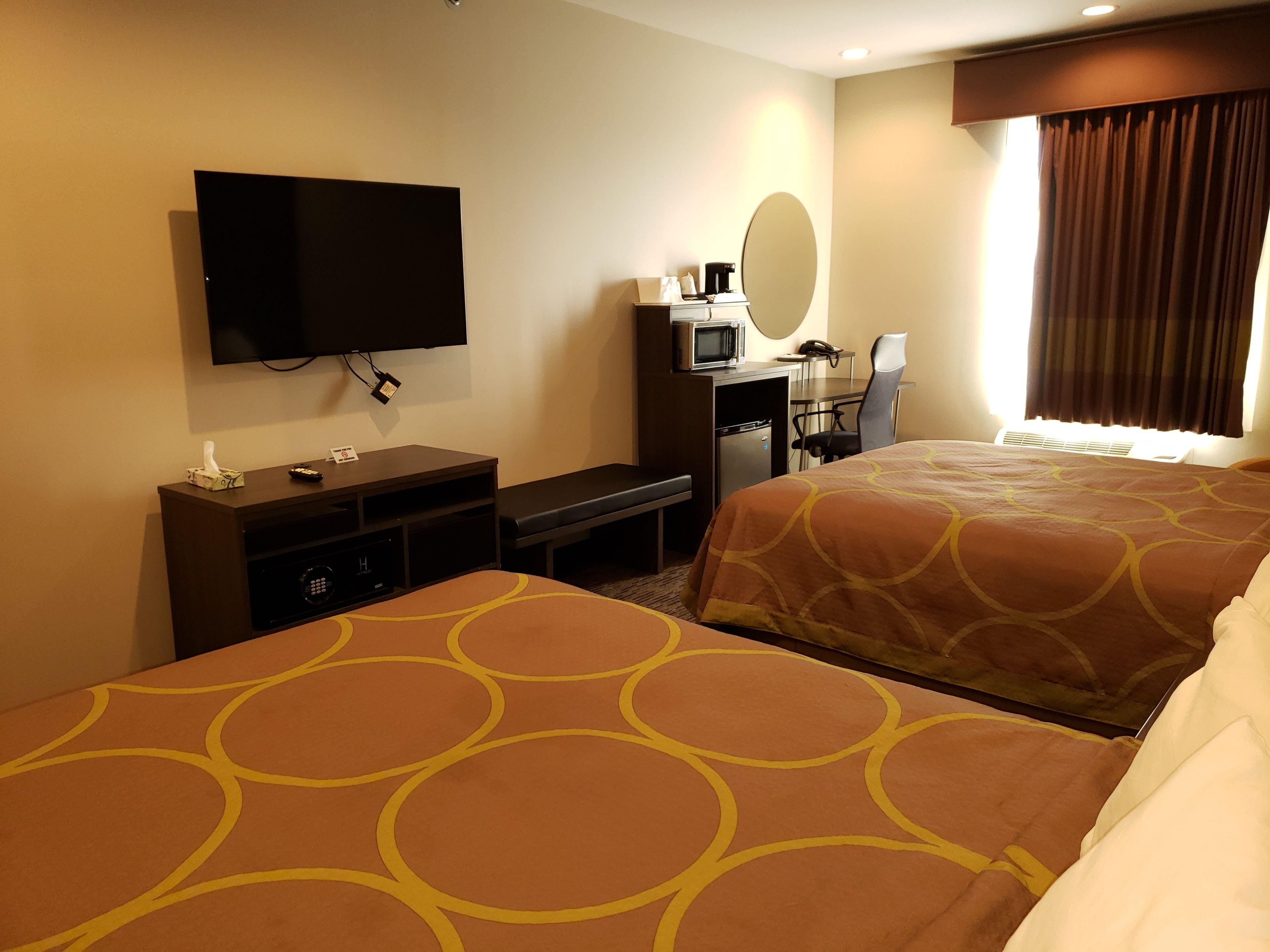A hotel room with two beds, a television, a desk with a chair, a microwave, and a small refrigerator.