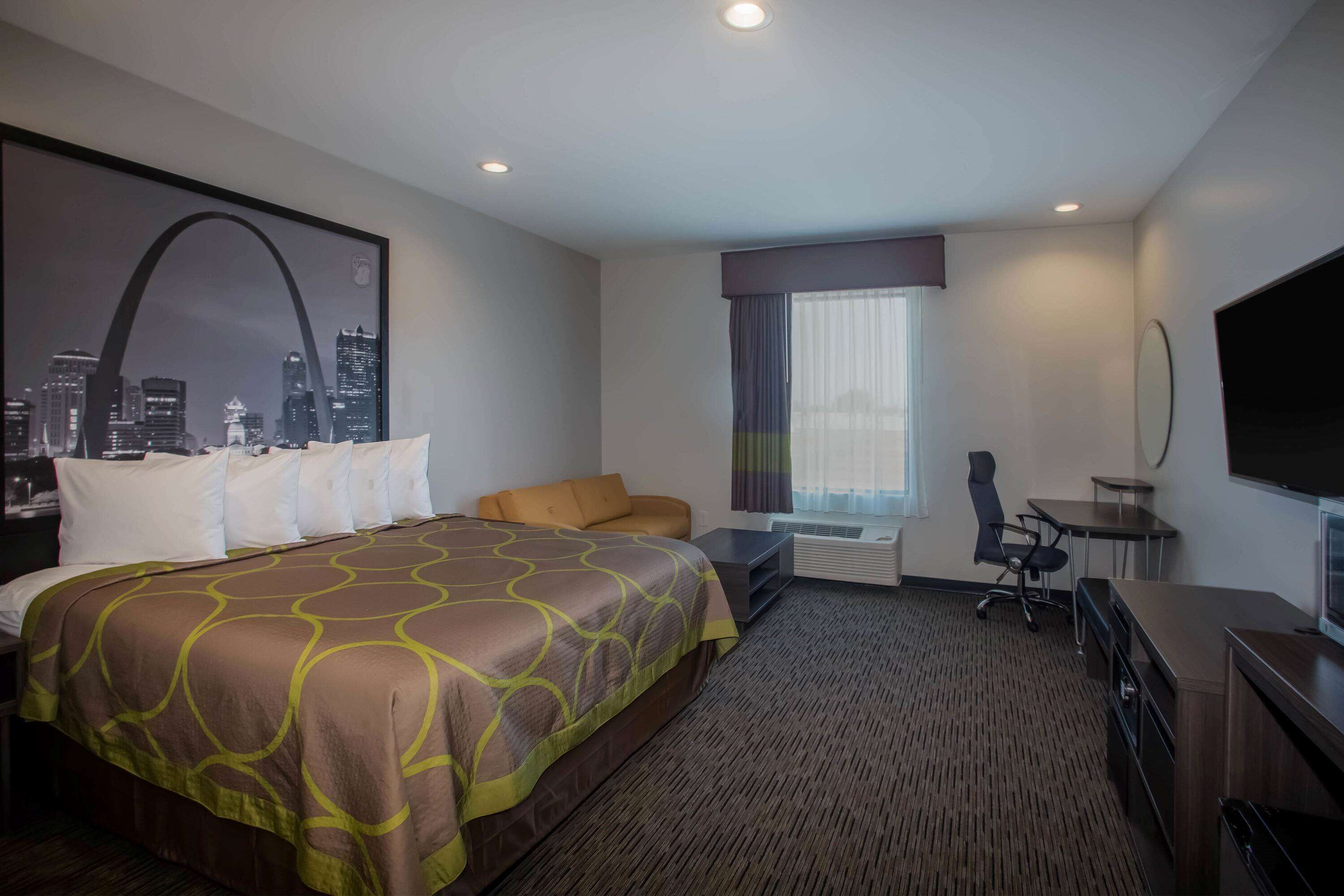 A hotel room with a large bed, a desk, a chair, a TV, and a window with curtains.