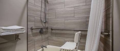 Un área de ducha con barra de apoyo, una silla blanca y un perchero para toallas.