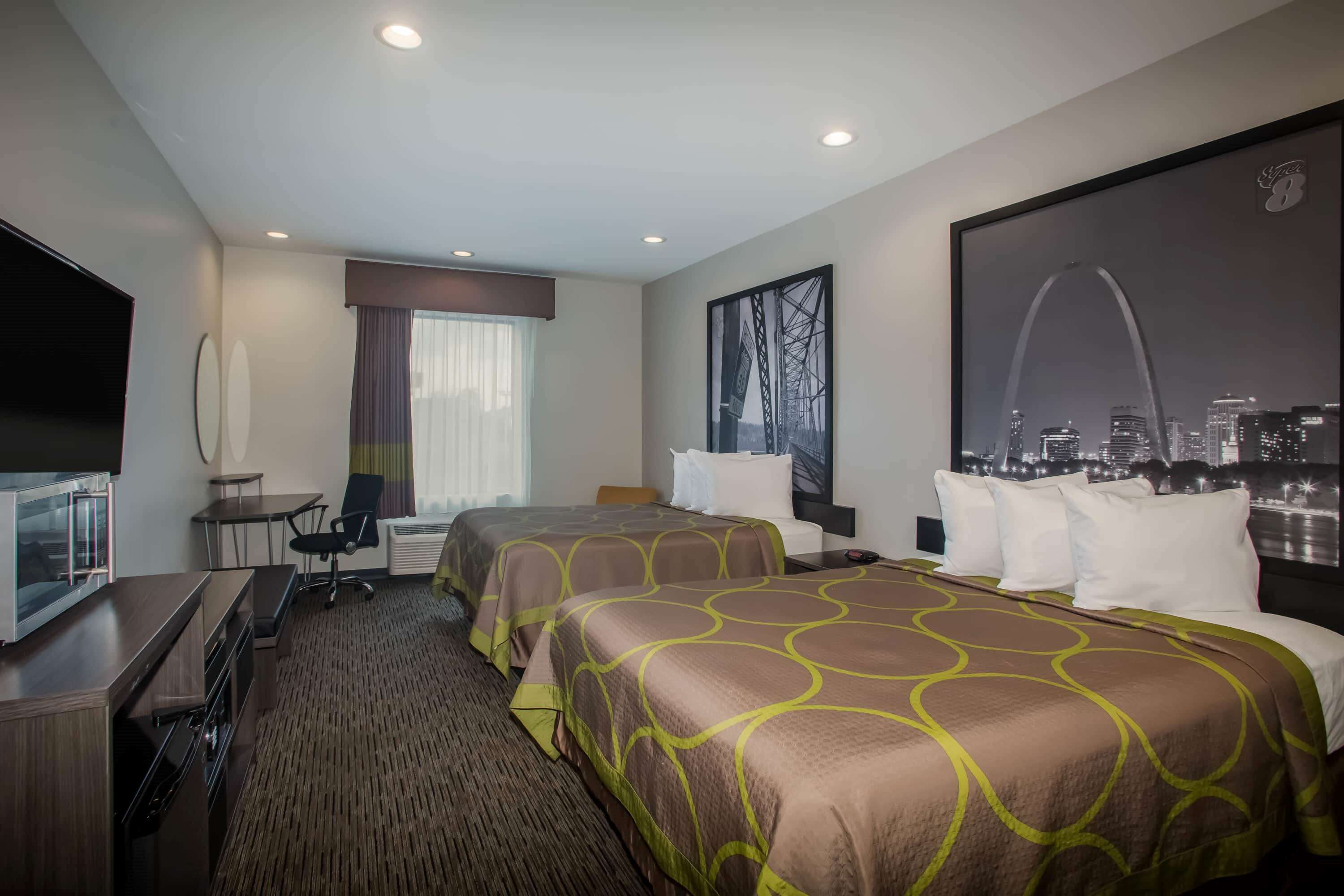 A hotel room with two beds, a desk, a TV, and a large window with a cityscape view.