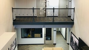 A spacious lobby with a herringbone floor, a central seating area, a chandelier, and a mezzanine level with a balcony.