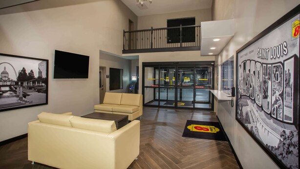 A hotel lobby with a sofa, a television, a staircase, and a wall with a 'Greetings from Saint Louis' sign.