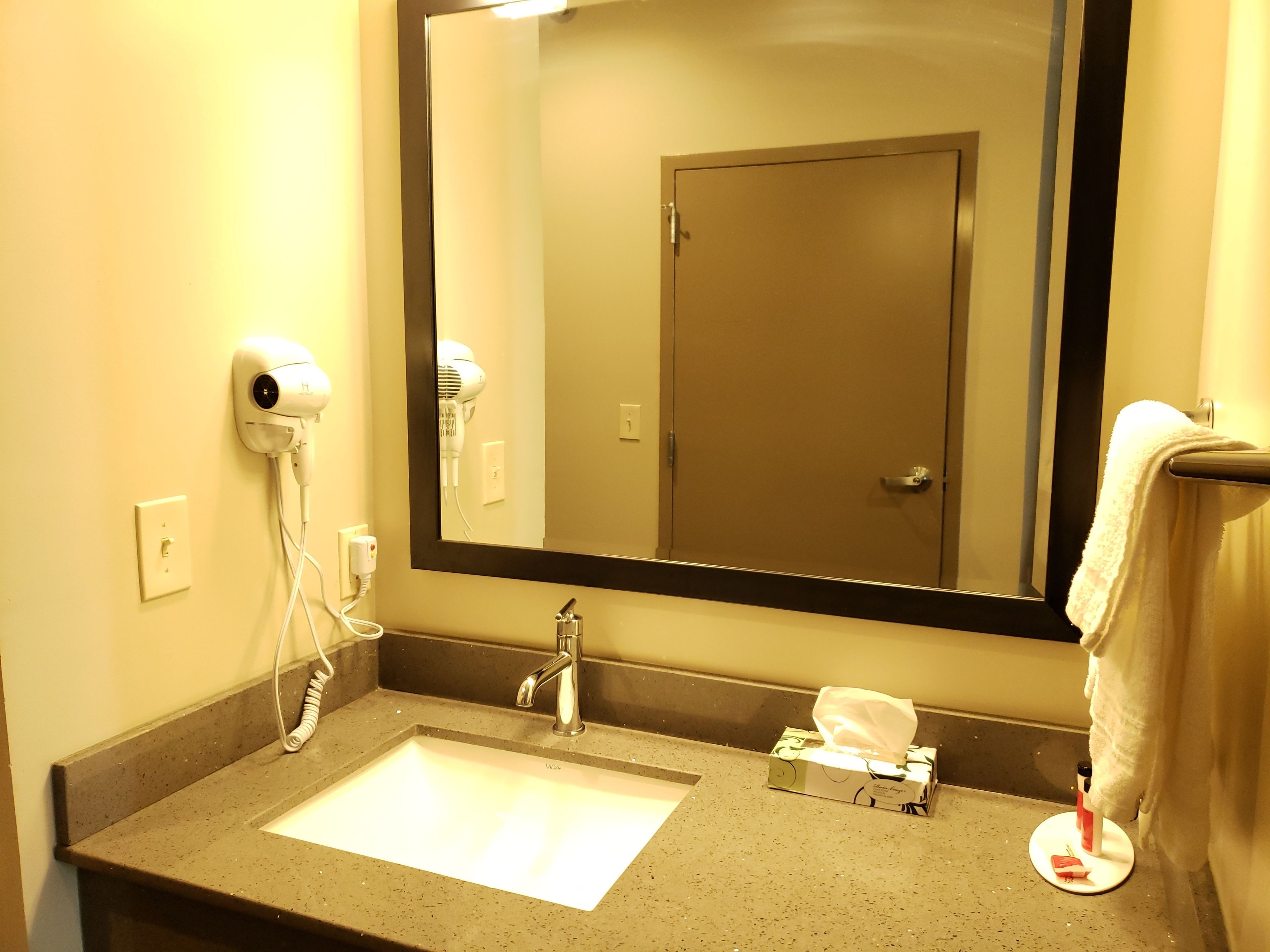 A bathroom with a sink, a hairdryer, a mirror, and a towel rack.