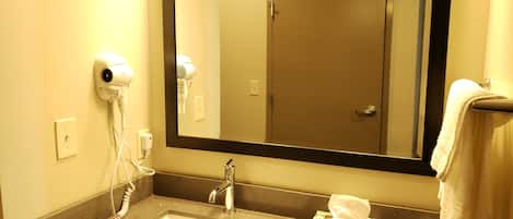 Un baño con lavamanos, secador de pelo, espejo y toallero.