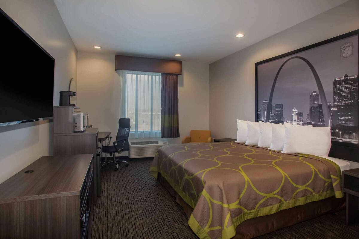Une chambre d’hôtel avec un grand lit, un bureau, une chaise, un téléviseur à écran plat et une fenêtre avec des rideaux.