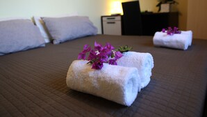 A neatly made bed with rolled white towels and purple flowers, a bedside table with a lamp, and a wall-mounted TV. - Verdeoliva Bed & Breakfast (Bari)