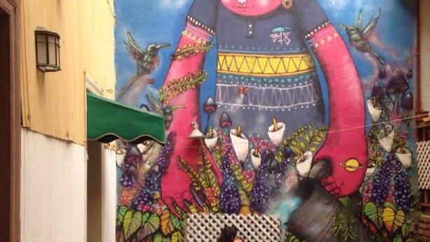 Un patio acogedor con un mural, zona de estar y una mesa con mantel a cuadros rojo y blanco.