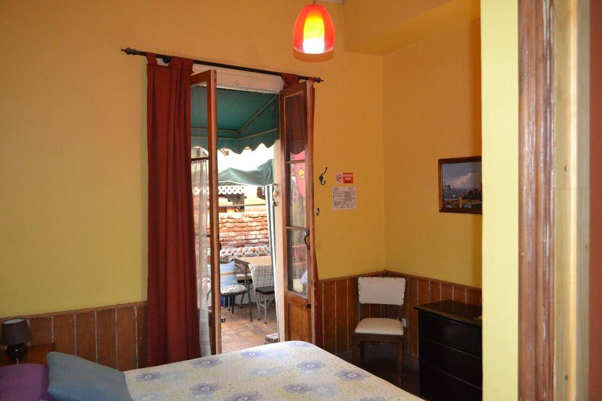 Una habitación con cama, escritorio, silla y mesa con sillas afuera.