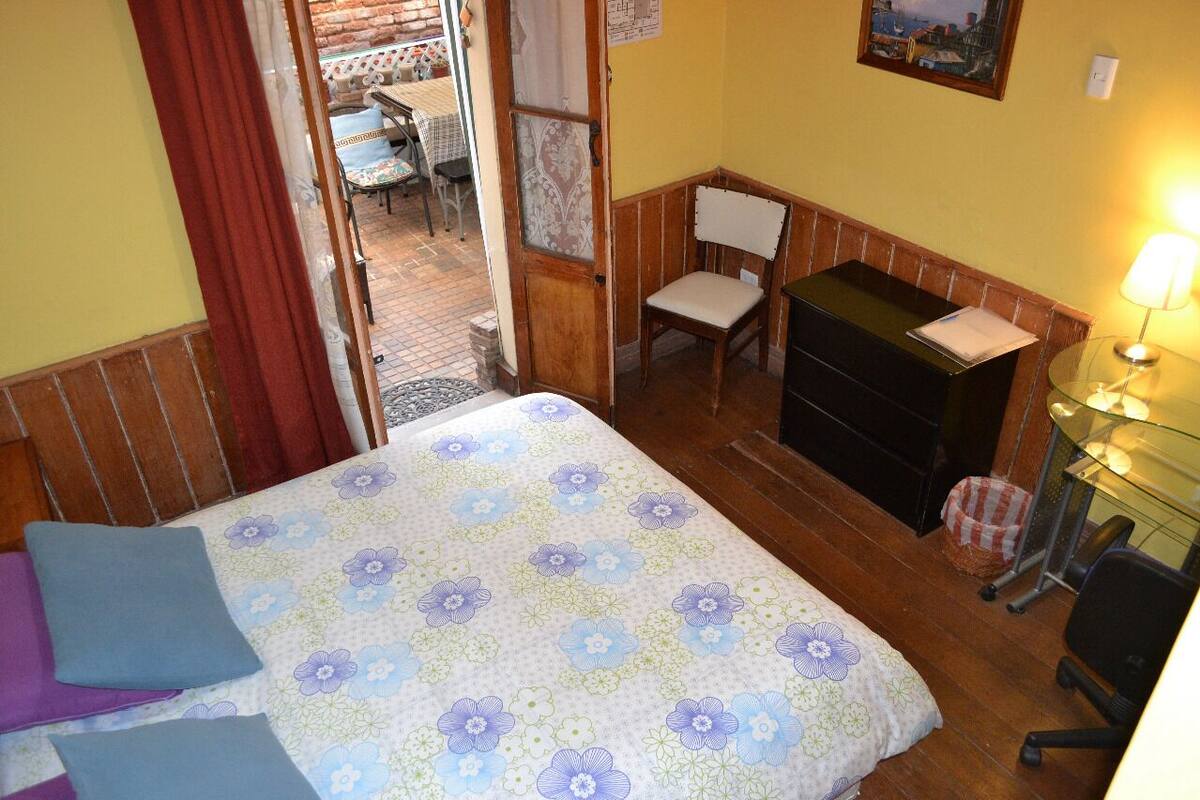Un dormitorio con cama, escritorio, silla y una mesita de noche con lámpara.
