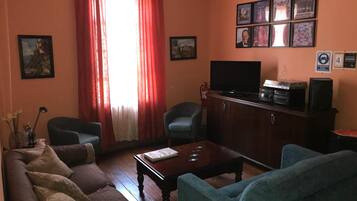 A living room with a sofa, two armchairs, a coffee table, a television on a cabinet, and framed pictures on the wall.