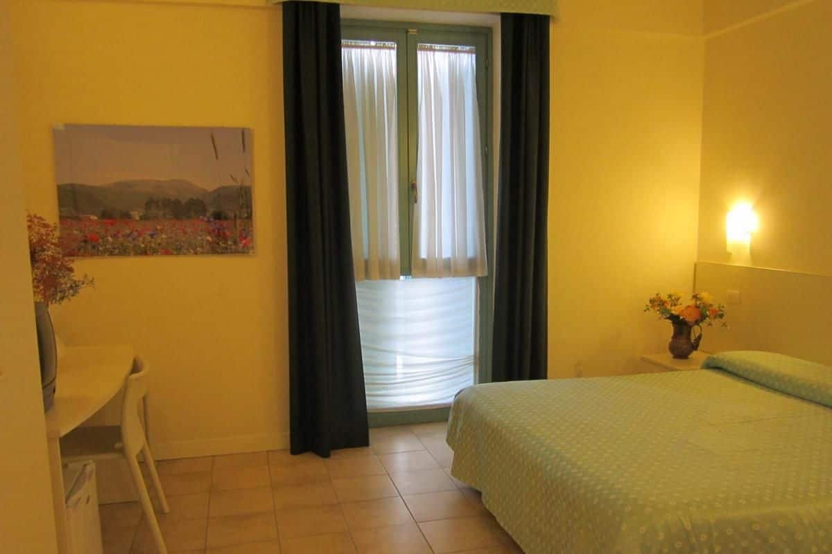 A room with a bed, a desk, and a window with curtains.