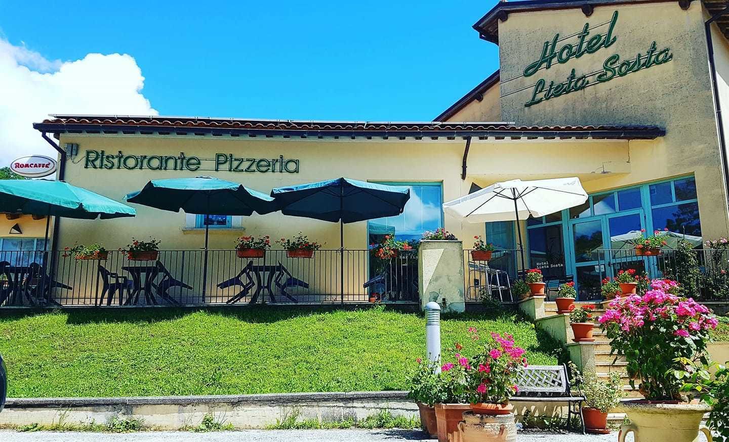 A building with a sign reading "Hotel Leila Sosa" and "Ristorante Pizzeria" with outdoor seating and umbrellas.