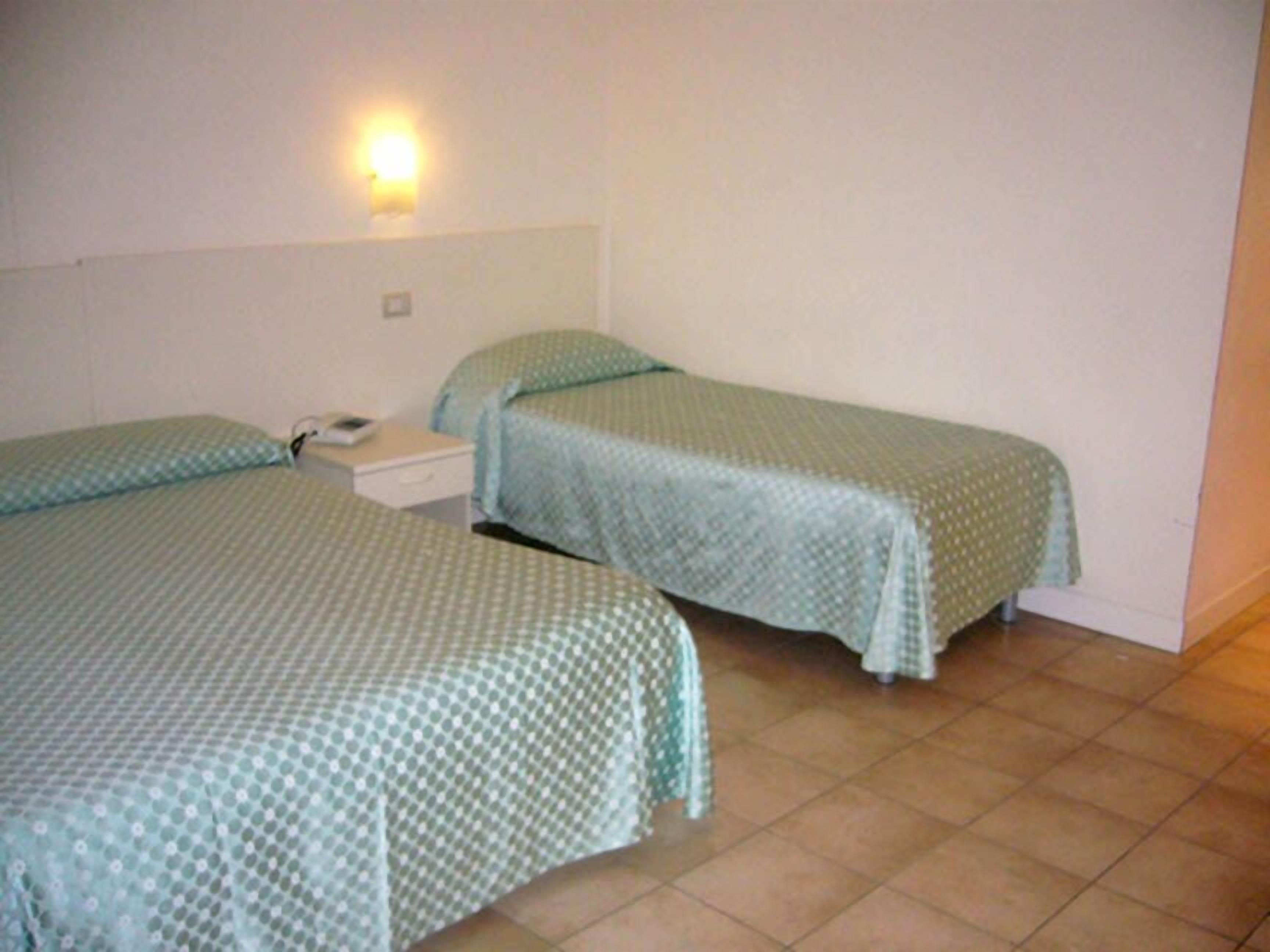 Ein Zimmer mit zwei Einzelbetten, einem Nachttisch und einer Wandleuchte.