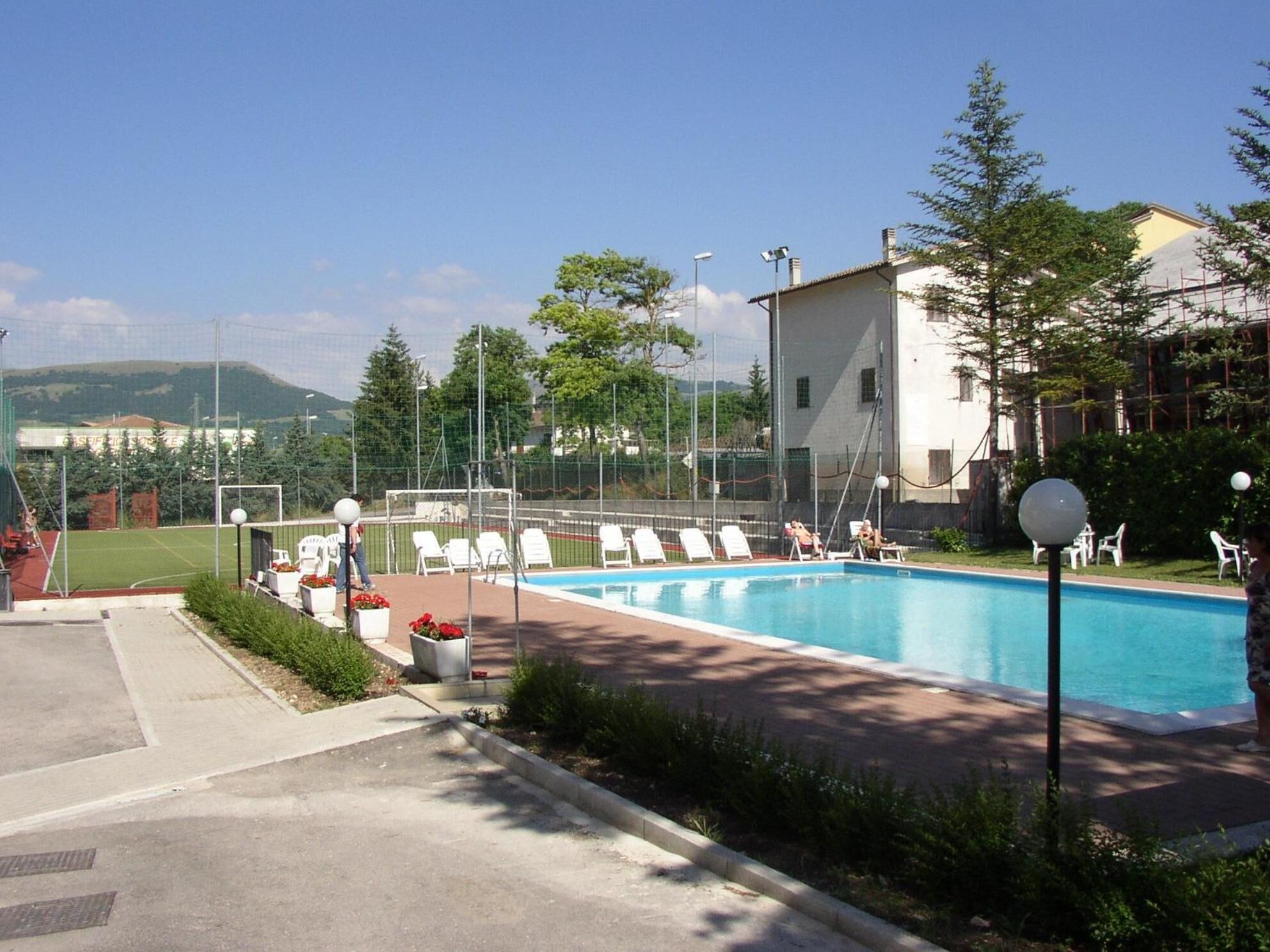 En swimmingpool med solstolar, en liten trädgårdsdel och en byggnad i bakgrunden.