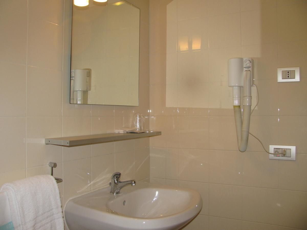 Un baño con lavamanos, espejo, toallero y un secador de pelo en un soporte de pared.