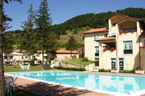 Un hotel con piscina, zona de estar exterior y un paisaje montañoso de fondo.