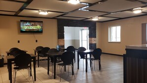 A restaurant interior with tables and chairs, a TV screen displaying 'WOODCHUCK', and a stone accent wall. - Travel Inn Of Sidney Ohio (Sidney)