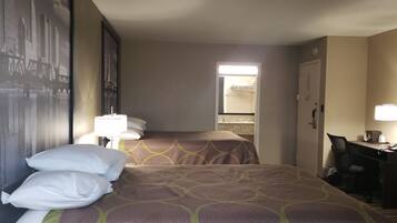 Habitación de hotel con dos camas, un escritorio y una silla. Se ve una ventana con vistas a edificios, una puerta que da al baño y un cartel con un paisaje urbano en la pared.