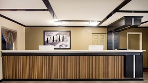 A reception desk with a wooden panel design, a framed picture on the wall, and a door to the right. - Travel Inn Of Sidney Ohio (Sidney)