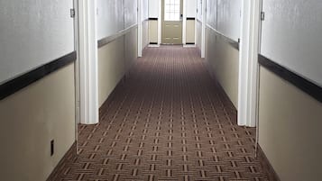 A long, narrow hotel corridor with patterned carpet, white walls, and doors on both sides.