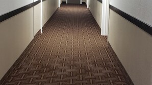 A long, narrow hallway with patterned carpet, white walls, and doors on both sides. - Travel Inn Of Sidney Ohio (Sidney)
