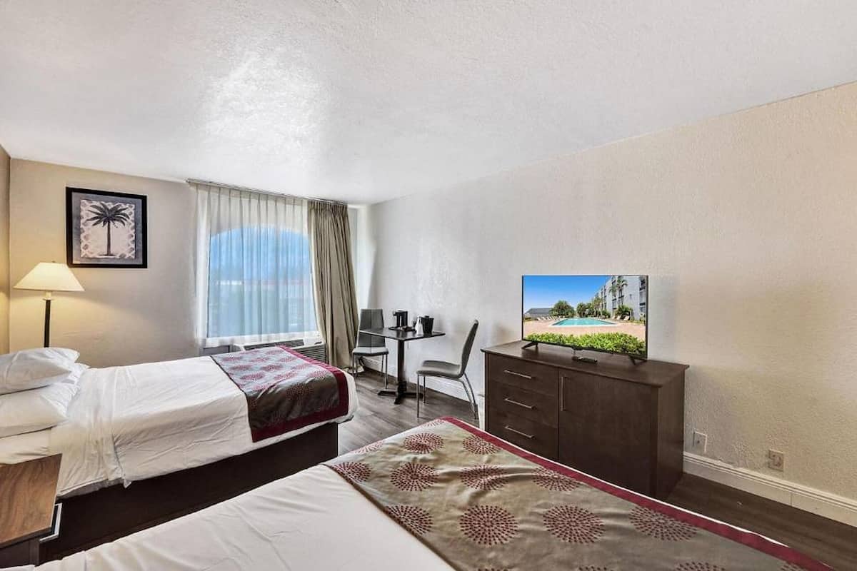 Une chambre d’hôtel avec deux lits, un bureau, une télévision et une vue sur la piscine.