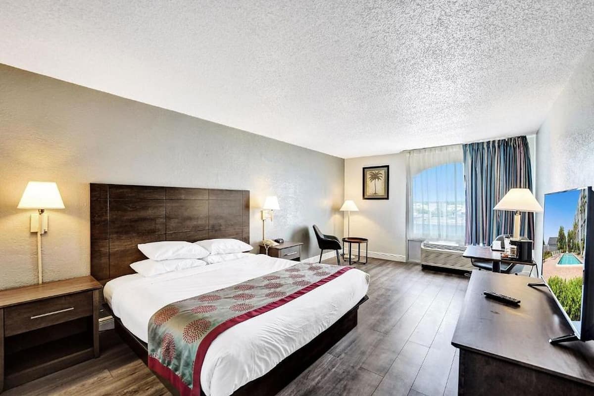 Une chambre d’hôtel avec un grand lit, deux tables de chevet avec des lampes, un bureau avec une chaise, une télévision et une vue sur la piscine.