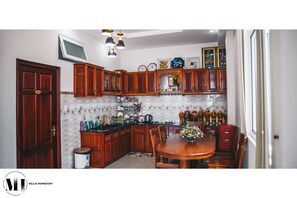 A kitchen with wooden cabinets, a dining table, and a TV mounted above the counter. - Villa Homestay Minh Hieu (Da Lat)