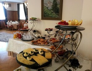 A buffet with various food items and drinks, including cheese, pastries, and fruits.