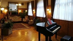 A cozy living room with a grand piano, wooden furniture, and warm lighting. - Hotel Adler (Sankt Georgen im Schwarzwald)