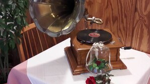 A vintage gramophone with a record player on a table, a bell-shaped horn, and a small glass container with a rose. - Hotel Adler (Sankt Georgen im Schwarzwald)