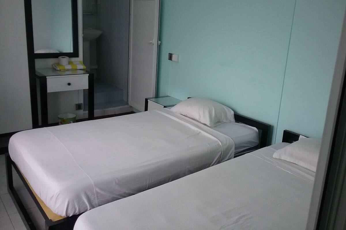 Slaapkamer met twee bedden, een spiegel, een klein tafeltje met een lamp en een badkamer zichtbaar door een geopende deur.