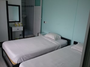 Une chambre avec deux lits, un miroir, une petite table avec une lampe, et une salle de bain visible à travers une porte ouverte.