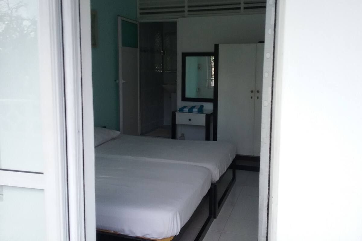 Een slaapkamer met twee bedden, een witte kast, een klein nachtkastje en een plafondventilator.