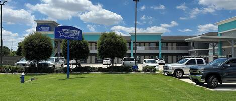 Un parking avec plusieurs voitures, un panneau indiquant « Americas Best Value Inn by Sonesta », et un bâtiment doté de balcons et d’un panneau « OUVERT MAINTENANT ».
