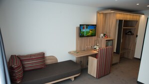 Een kleine hotelkamer met een bed, een bureau, een televisie en een inloopkast.