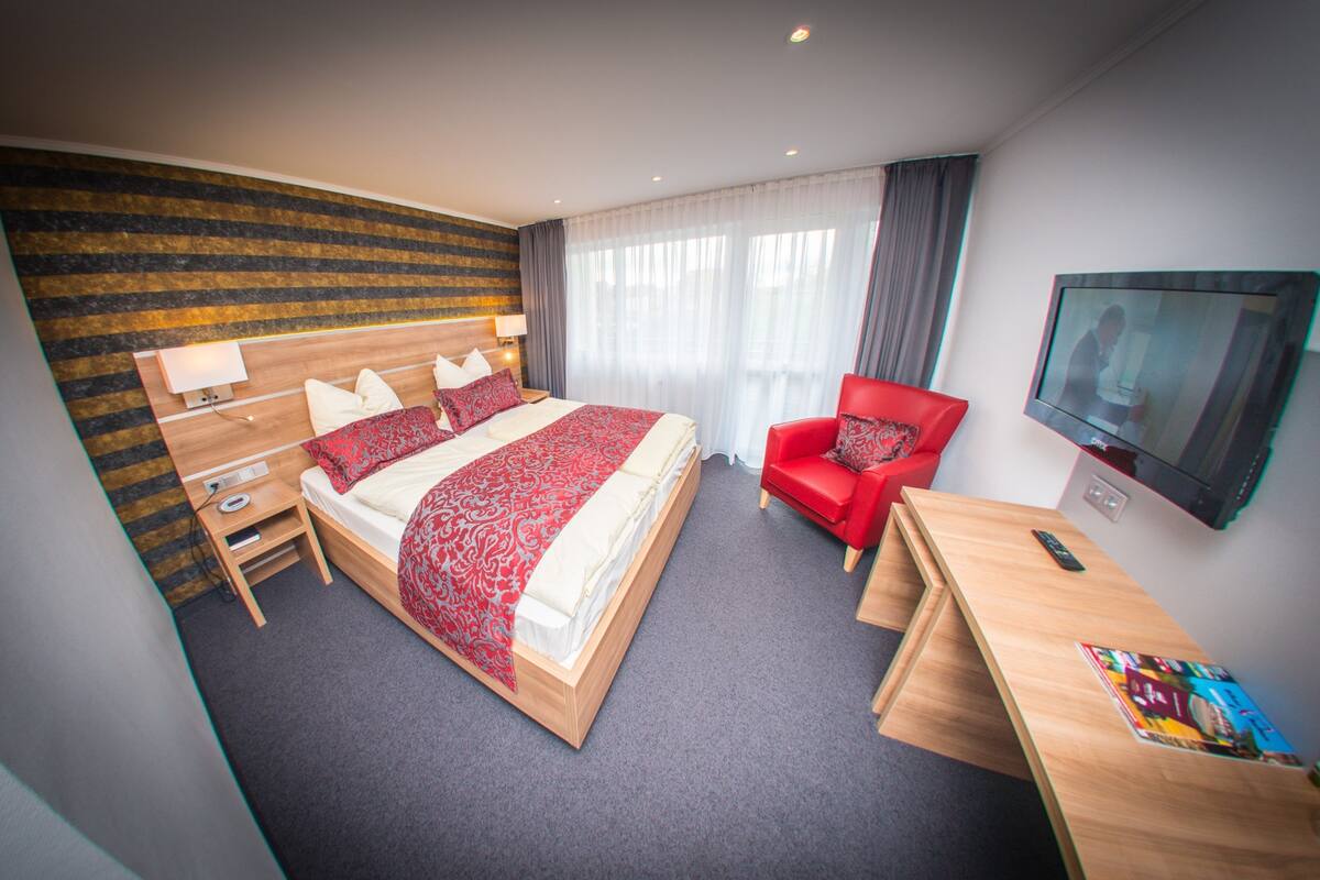 Quarto de hotel com cama, secretária, cadeira, televisão e televisão montada na parede.