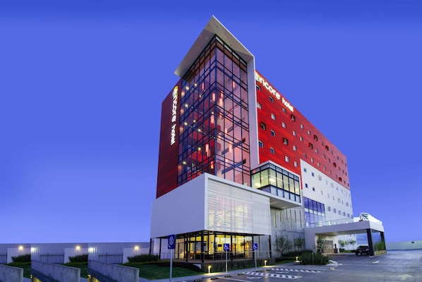 A modern hotel with a red and white facade, multiple floors, and a covered entrance area.