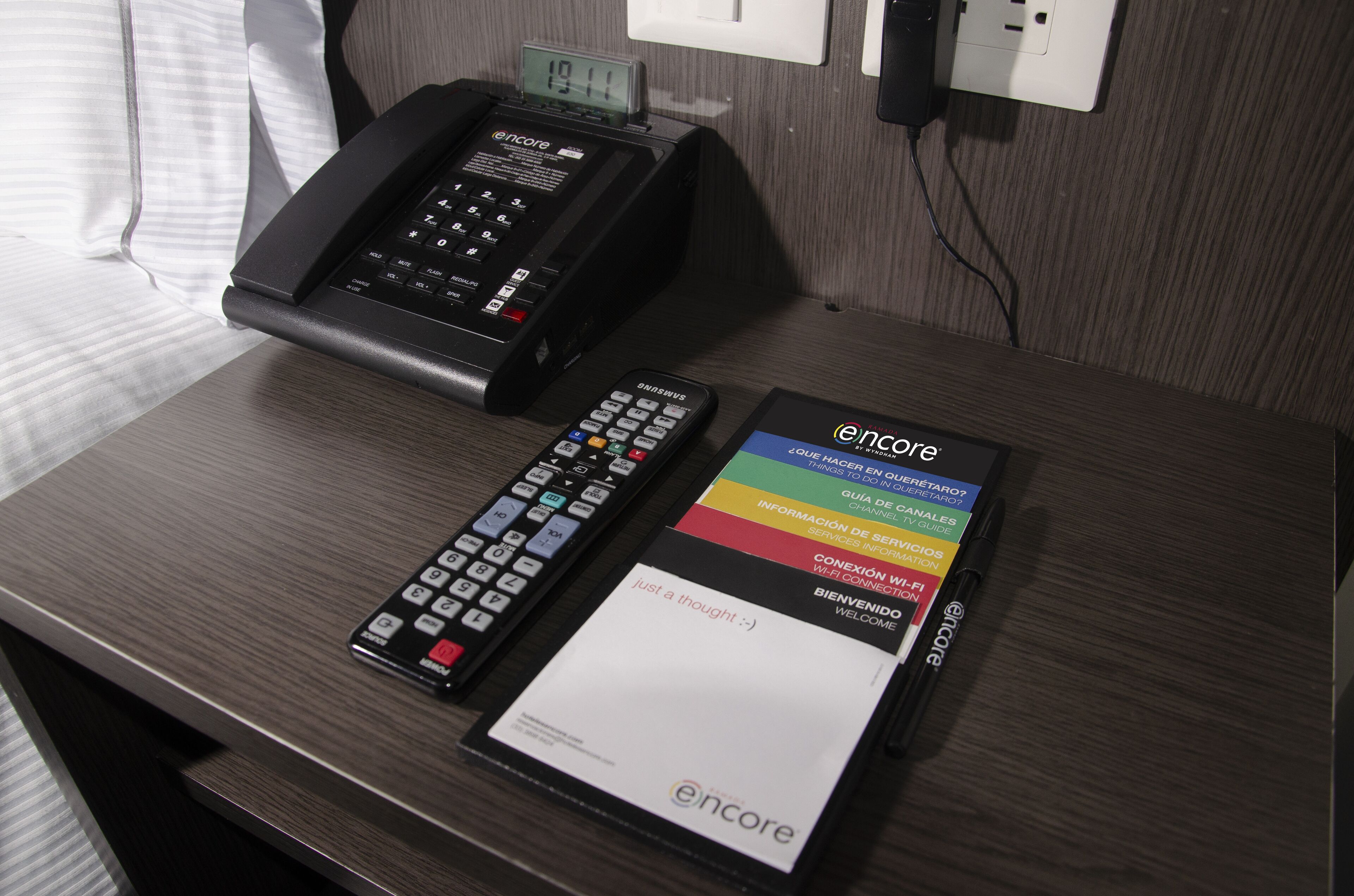 Habitación de hotel con escritorio, teléfono fijo, control remoto y una tarjeta de bienvenida.
