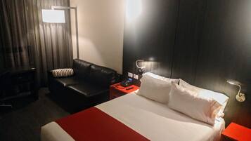 Een hotelkamer met een groot bed, een zwarte leren bank, een rode bijzettafel en een aan de muur bevestigde televisie.