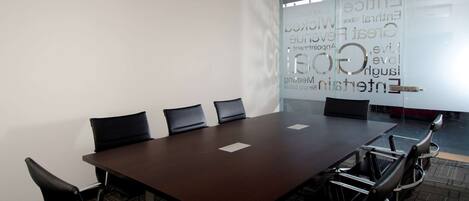 A conference room with a large table, four chairs, and a glass wall with word clouds.
