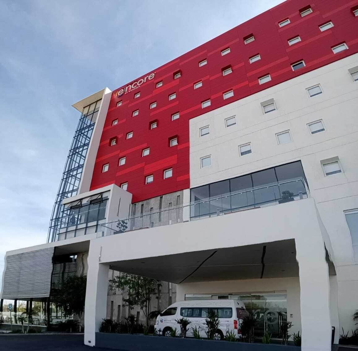 A modern hotel with a red and white facade, multiple floors, and a covered parking area.