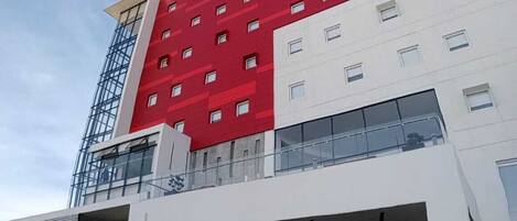 A modern hotel with a red and white facade, multiple floors, and a covered parking area.