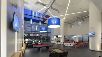 Un espace intérieur moderne doté d’une table de billard, d’un baby-foot et d’un bar avec plusieurs écrans.