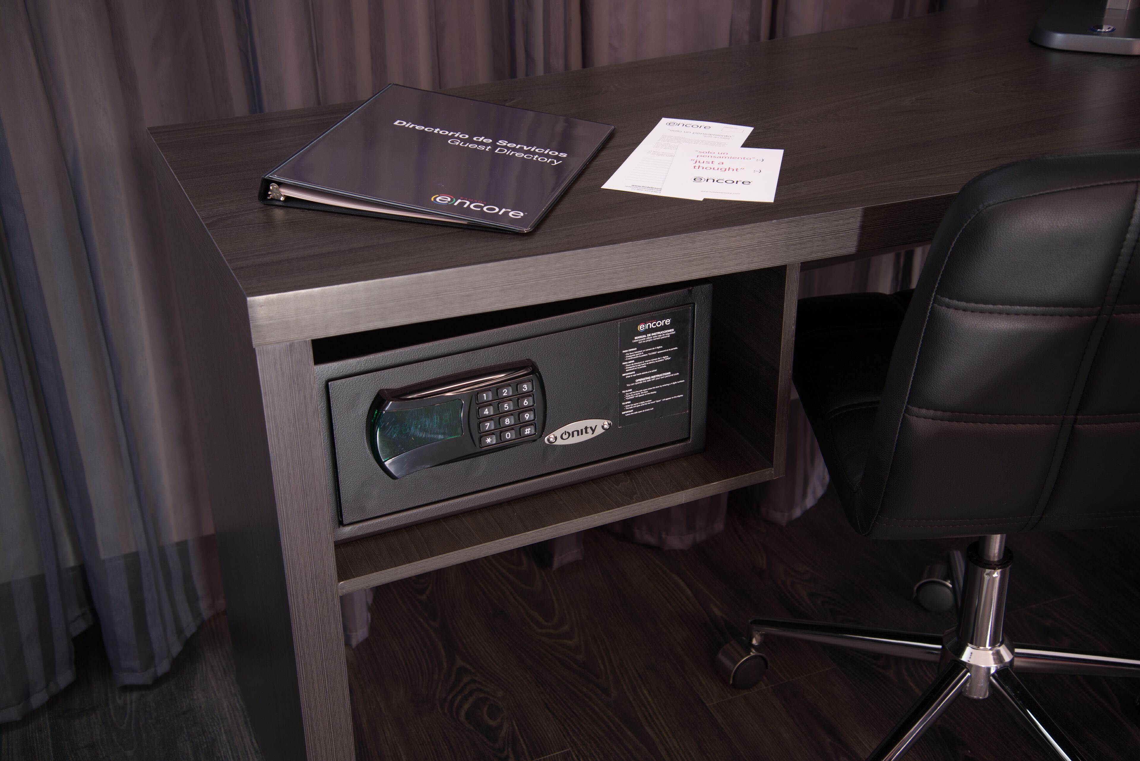 Escritorio con acabado de madera oscura, una silla negra y un minibar integrado con ranura para llave.