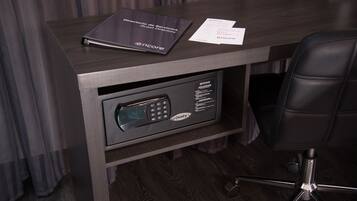 Escritorio con acabado de madera oscura, una silla negra y un minibar integrado con ranura para llave.