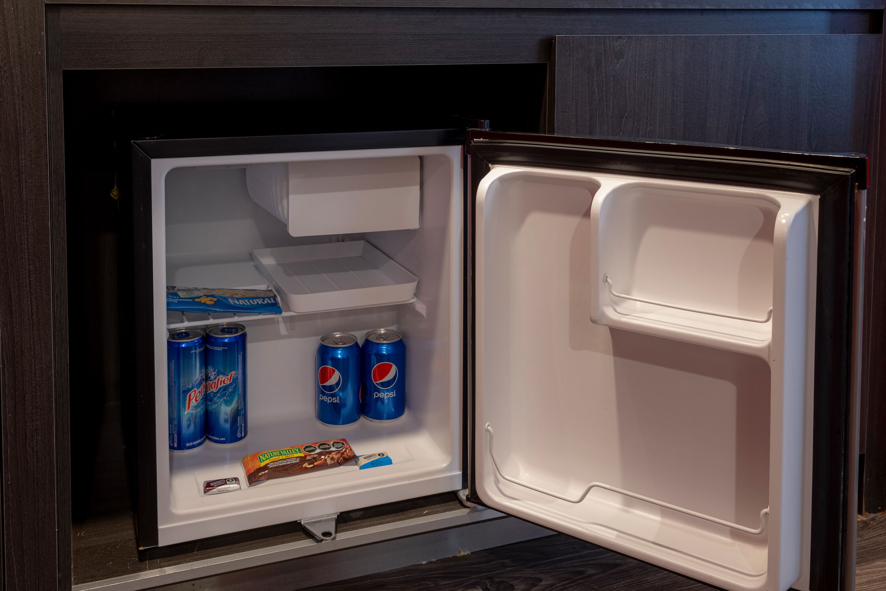 Jääkaapissa on kaksi hyllyä. Ylemmällä hyllyllä on kaksi Perrier-limsatölkkiä ja kaksi Pepsi-limsatölkkiä, ja alemmalla hyllyllä on suklaapatukka ja paketti paperiliinoja.